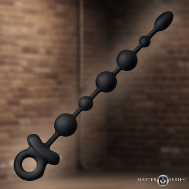 A black silicone beaded anal toy with a ring handle, shown diagonally against a blurred brown brick wall background. The 'MASTER SERIES' logo is visible in the bottom right corner.