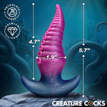 A pink and blue novelty cock product displayed on a rock with overlaid dimension lines showing 4.7 inches tall, 1.