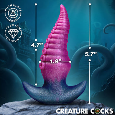 A pink and blue novelty cock product displayed on a rock with overlaid dimension lines showing 4.7 inches tall, 1.