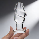 Hand holding clear glass penis butt plug highlighting smooth curved shape and flared base for secure use