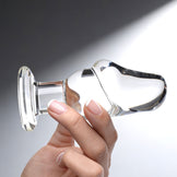 Side view of transparent glass butt plug in hand showing ergonomic curve and rounded tip for comfortable insertion