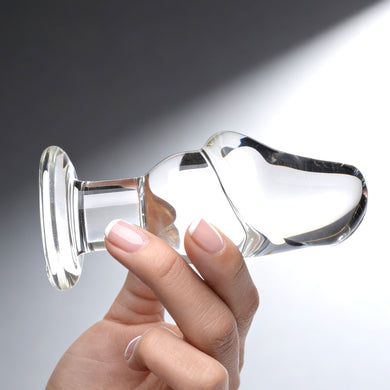 Side view of transparent glass butt plug in hand showing ergonomic curve and rounded tip for comfortable insertion