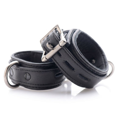 Pair of black padded locking wrist cuffs with adjustable buckles and metal D-rings displayed on a white background