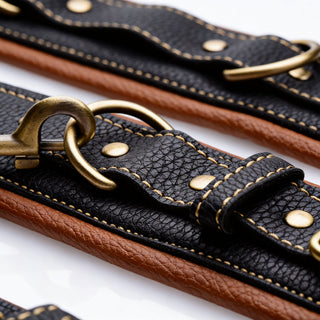 Close-up of Coax collar to wrist restraints showing textured faux leather, reinforced stitching, antique gold rings, and chain clips