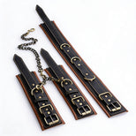 Coax collar to wrist restraints set with black and brown padded faux leather cuffs, antique gold hardware, and detachable connecting chains