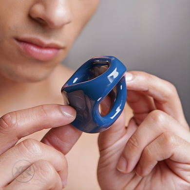 Close-up of blue dual cock and ball ring held in hand, showing smooth finish and ergonomic shape with dual openings for comfortable fit