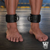 Leather Ankle Cuffs locked on bare ankles, black leather with embossed chevron shield and D-rings