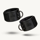 Leather Ankle Cuffs pair on white, black leather with Velcro closures and gunmetal D-rings