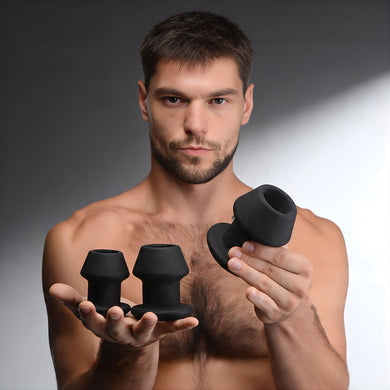 Man holding three black silicone hollow anal dilators showing graduated sizes for progressive training and stretch