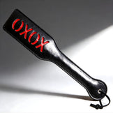 Black imprint spanking paddle with red OXOX lettering, glossy finish with wrist strap for secure grip and impact play