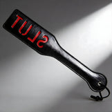 Black imprint spanking paddle with red SLUT lettering, firm paddle design with wrist strap for impact and marking
