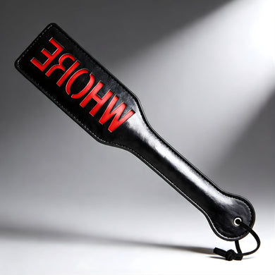 Black imprint spanking paddle with bold red WHORE lettering, smooth striking surface with wrist loop for control