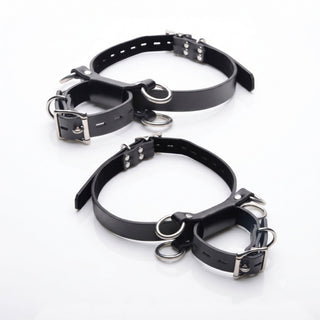 Pair of adjustable black thigh and ankle restraint cuffs with multiple attachment rings and polished metal buckles