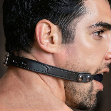 Locking silicone ball gag fastened with its leather strap for BDSM mouth restraint
