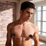 Male model wearing black vibrating nipple suckers with metallic accents, demonstrating fit and placement on the chest