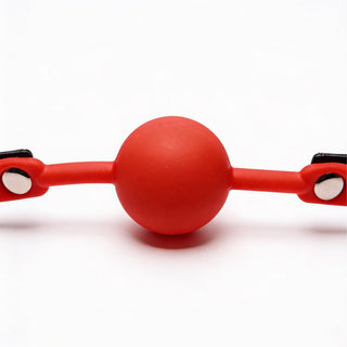 Close-up front view of bright red silicone comfort ball attached to a black faux leather gag strap