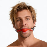 Male model wearing a black faux leather gag with bright red silicone comfort ball centered between the lips
