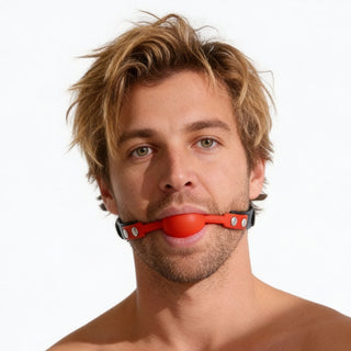 Male model wearing a black faux leather gag with bright red silicone comfort ball centered between the lips