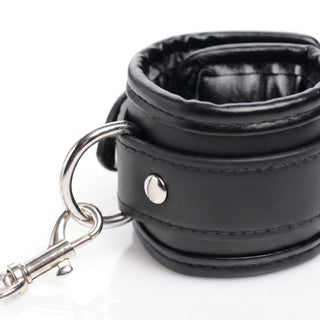 Detailed view of a padded black restraint cuff featuring a metal D-ring, swivel clasp, and reinforced rivet construction