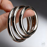 Close-up of Steel Cock Rings Set held in hand, showing smooth polished metal finish and solid construction in graduated sizes