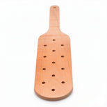 Front view of a perforated wooden impact paddle featuring a rounded striking head and smooth handle