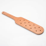 Light wood spanking paddle with perforated striking surface and ergonomic handle displayed on a white background